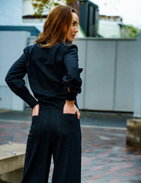 Woman wearing a black DEVOI Susie shirt in linen with a long wrap tie at the waist. Back view on model