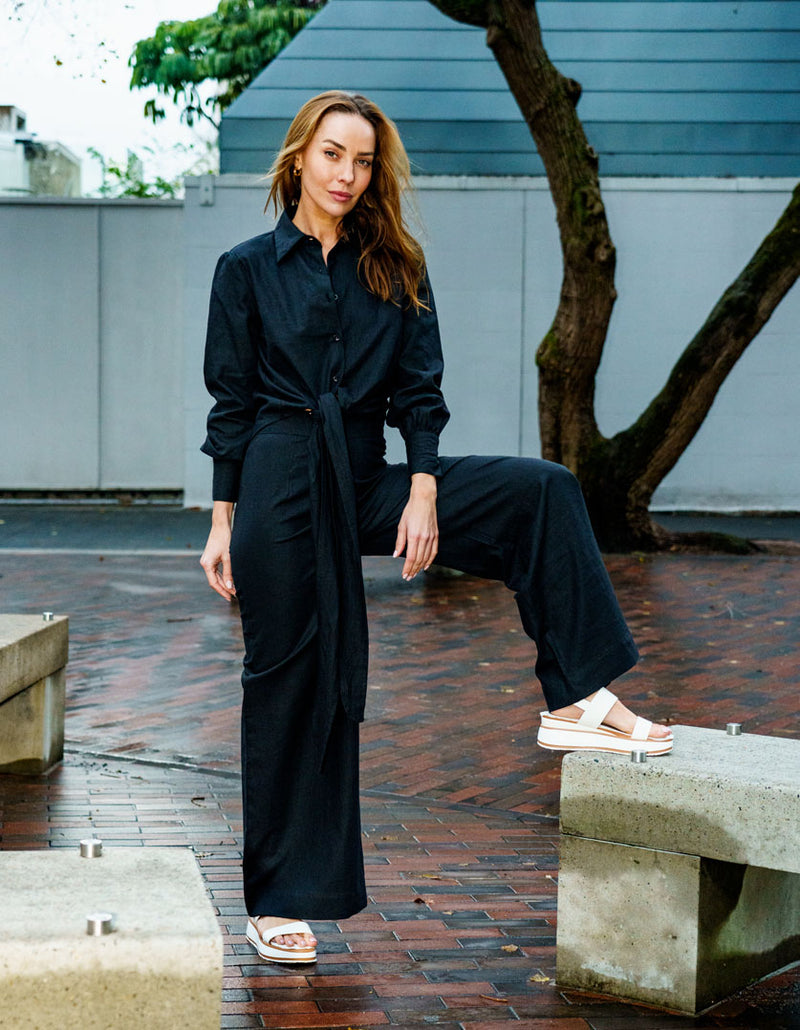 Woman wearing a black DEVOI Susie shirt in linen with a long wrap tie at the waist. Front view outside.