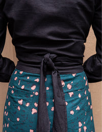 Woman wearing a black long-sleeve shirt with a wrap around tie at the waist with pink leopard print pattern pants in linen. Back view