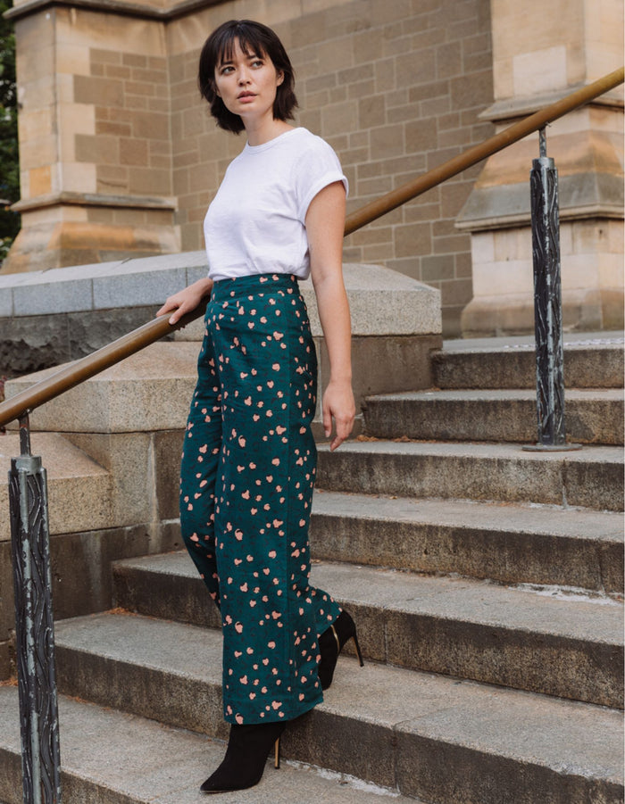 Woman in a white top and DEVOI green patterned pants in leopard printed linen standing on stone steps outdoors.