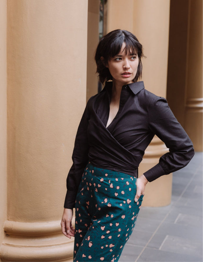 Woman wearing a black DEVOI Susie shirt in linen with a long wrap tie at the waist. Side front