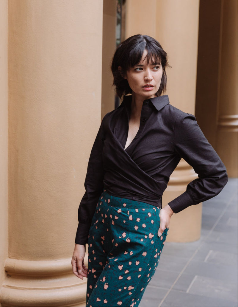 Woman wearing a black DEVOI Susie shirt in linen with a long wrap tie at the waist. Side front