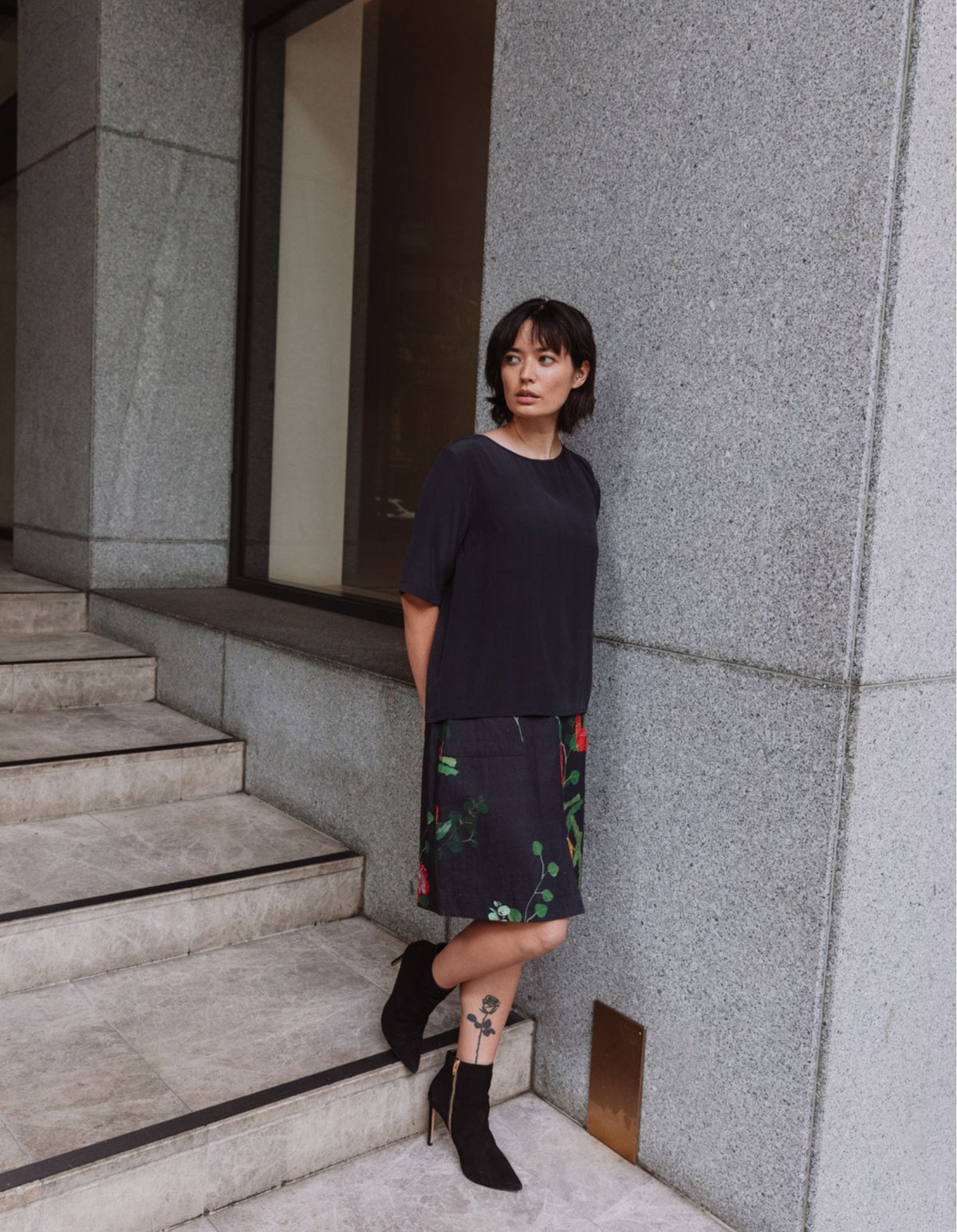 Model wearing a DEVOI black Lise top in plain black silk crepe. Side front full length view.