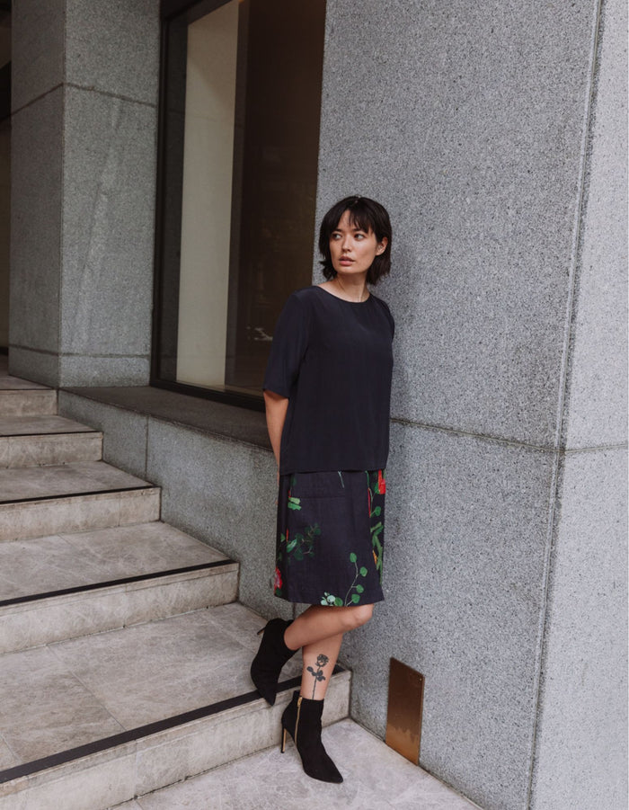 Model wearing a DEVOI black Lise top in plain black silk crepe. Side front full length view.
