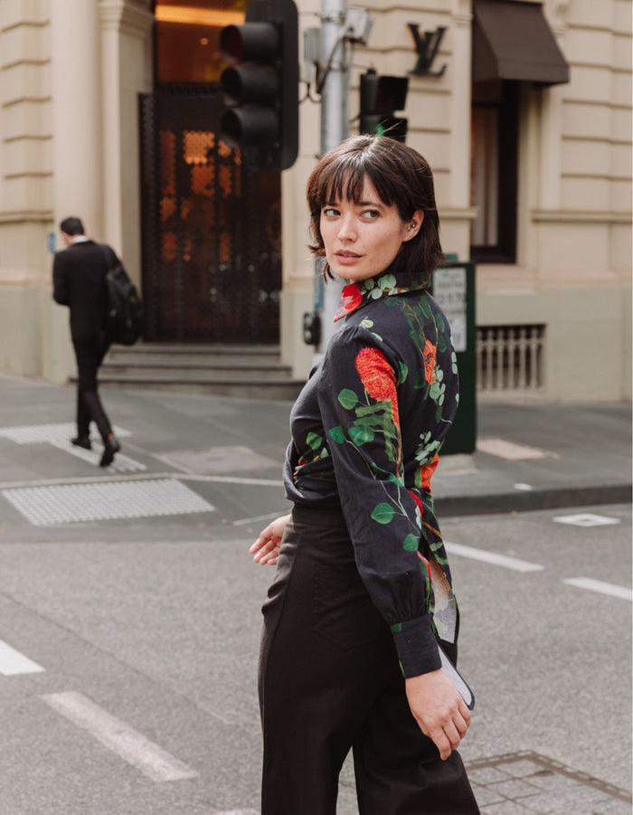 Model wearing the DEVOI Susie Shirt in black Wild Blooms floral printed linen, with waist ties and long cuffs. Side back view