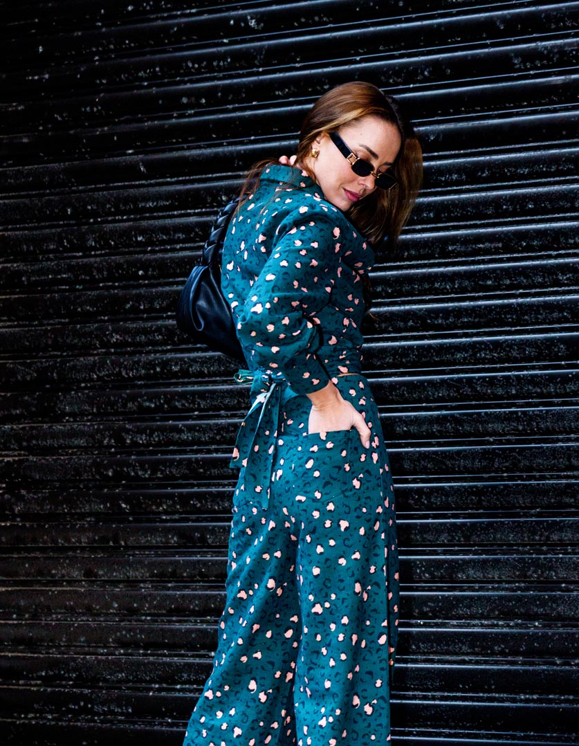 Woman wearing a teal wrap shirt with a leopard printed pattern in linen, against a dark background