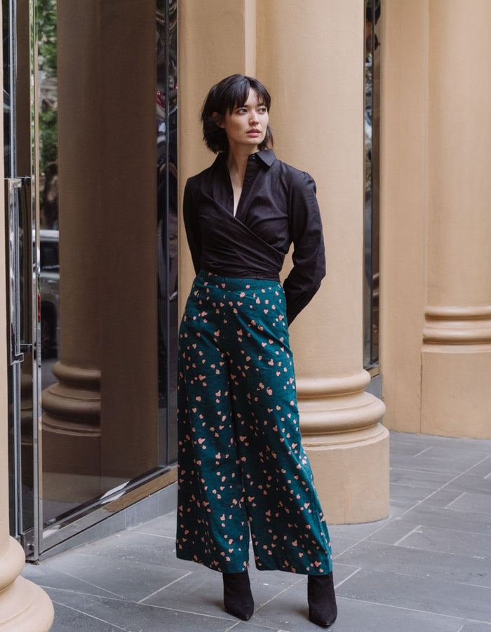 Woman in a DEVOI black wrap shirt and teal patterned pants in linen standing in front of classical columns.