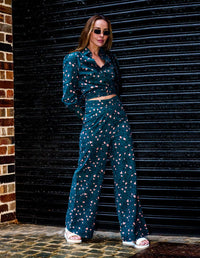 Woman wearing a DEVOI teal leopard printed wrap shirt and long pants, standing against a black shutter.