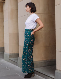 Woman wearing a white t-shirt and DEVOI Jessie teal patterned pants in linen standing against a beige wall.