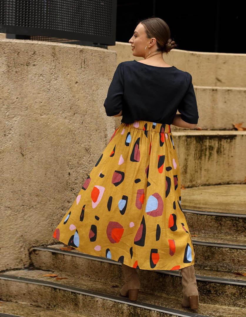 DEVOI Kathleen skirt in new print Mustard Sauros. Elastic waist and pockets. Skirt falls just below the knee. Drawstring tie at front waist. Back view.