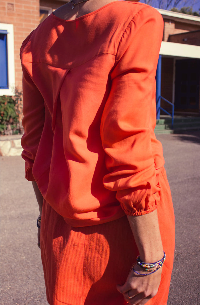 DEVOI Everleigh top blouse in bright orange. Our Everleigh is loose fitting long sleeved top with a folded cross over detail at the front, and flattering v-neckline, full length sleeves and elasticated cuffs. The back has an elegant fold below the yoke panel.