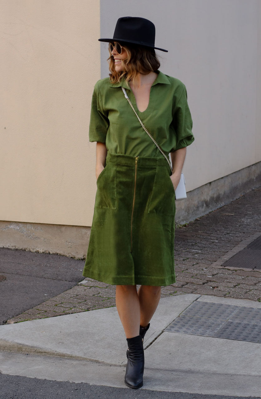 DEVOI Maya skirt in moss green colour. A-line shape with metal zip detail down the front of the skirt with a split at the front hem. Front and back pockets. Back waistband is elasticated. Front view