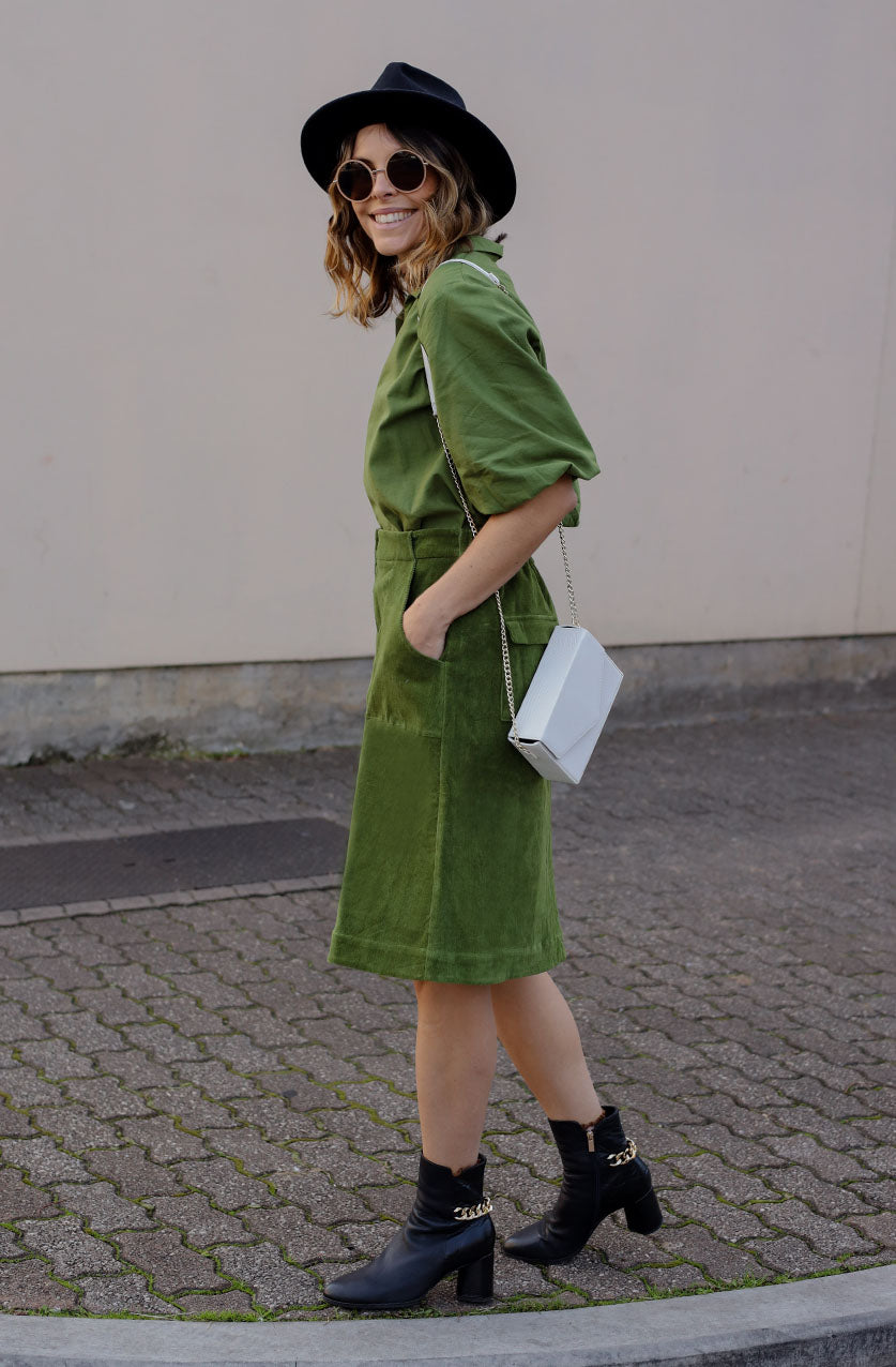 DEVOI Maya skirt in moss green colour. A-line shape with metal zip detail down the front of the skirt with a split at the front hem. Front and back pockets. Back waistband is elasticated. side view